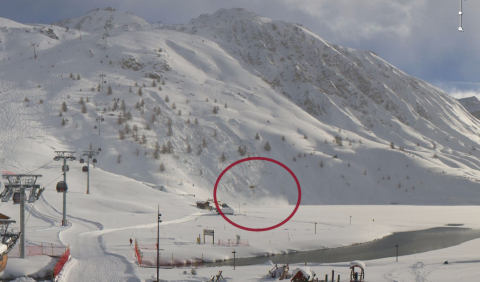 Webkamera képe a baleset idején. Tignes, Le Lac rész. A hegyoldalon látható a lavina nyoma, alatta a tó, amelybe a lavina sodorta a síelőt. Bekarikázva a mentőhelikopter.