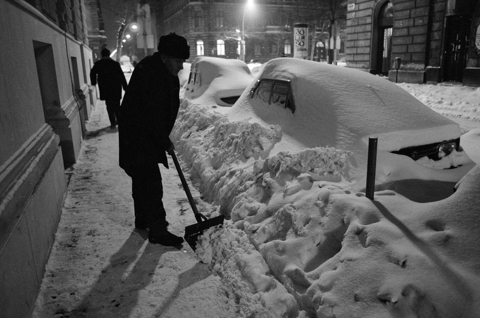 Budapest, 1987. január 14. Egy férfi havat lapátol az utcán hajnalban. Az intenzív havazás miatt az utcán parkoló autókat belepte a hó, a kenyérellátás akadozik. Fotó: Pataki Gábor, MTI