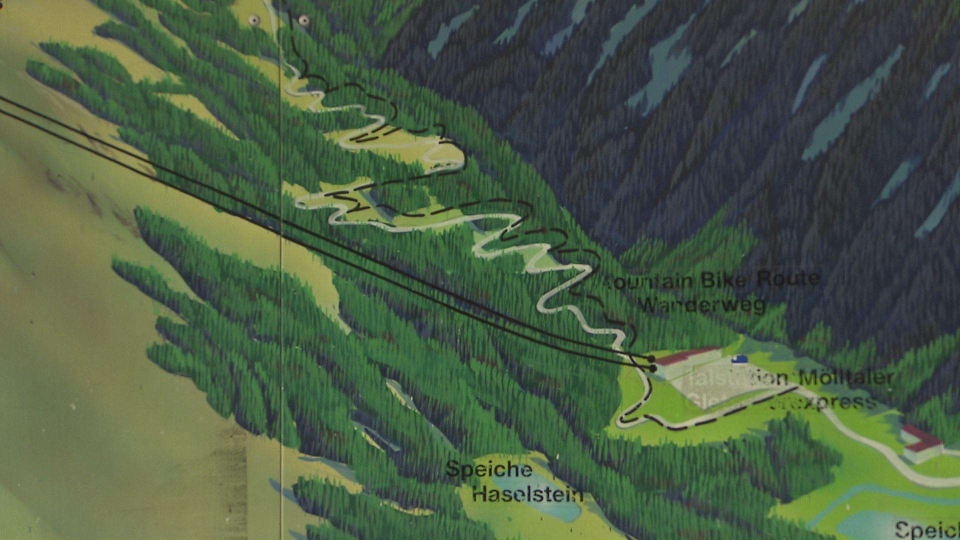 A tervezett pálya nyomvonala (fehérrel), a középső liftállomás és a völgyállomás között. Szaggatott feketével a jelenlegi hegyi út.